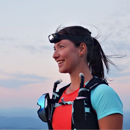 A woman trail runner wearing a hydration vest and headlamp
