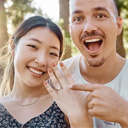 A couple smiles while pointing to her engagement ring