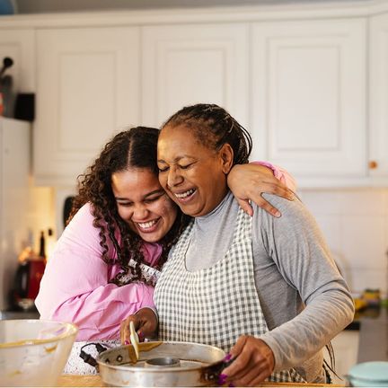 A woman and her mother hug while stirring a bowl in a kitchen