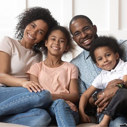 A family of four sits on a couch, smiling