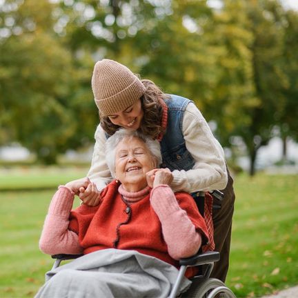 A woman in a coat and hat hugs her grandmother in a wheelchair