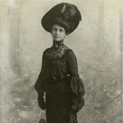 An old photo of an elegant woman in a black dress and fancy hat