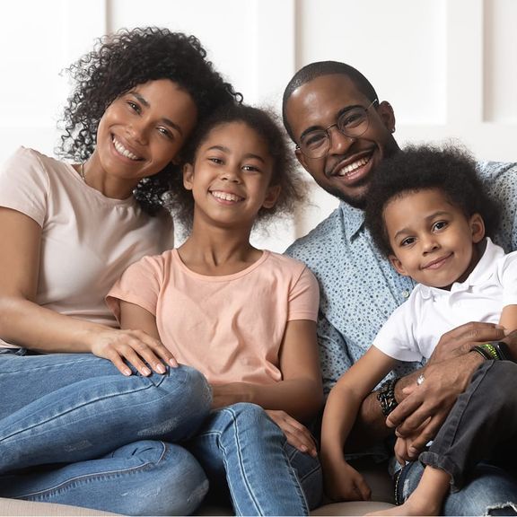 A family of four sits on a couch, smiling